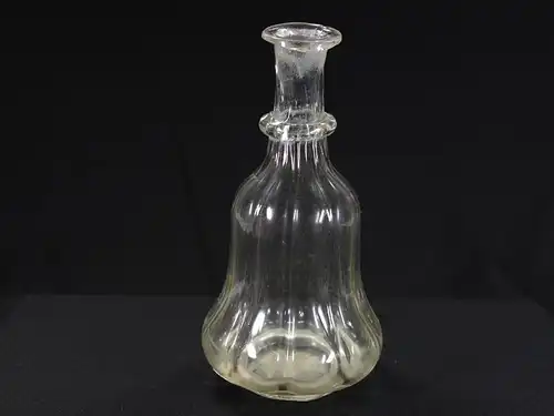 Glasflasche, 18. Jh., leicht gelblstichiches Glas, glockenförmiger Körper spiralförmig gedreht mit Abriß, schräger Hals mit angesetzten Glasknoten. H: 17 cm