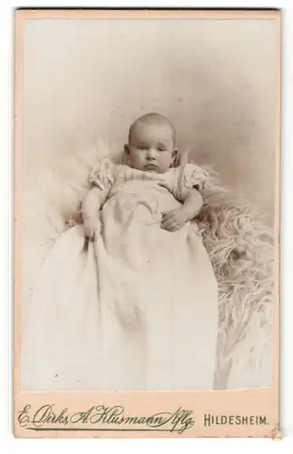 Fotografie E. Dirks, Hildesheim, Baby in langem Kleid auf Fell liegend