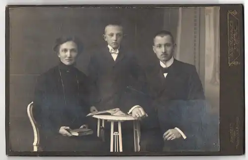 Fotografie Rudolf Neubauer, Bielefeld, Niedernstrasse 17 II, Portrait bürgerliches Paar und Sohn mit Zeitung am Tisch