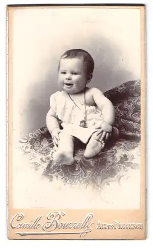 Fotografie Camille Bourrelly, Aix-en-Provence, Portrait Kleinkind im Kleid mit Kette sitzt auf einem Teppich