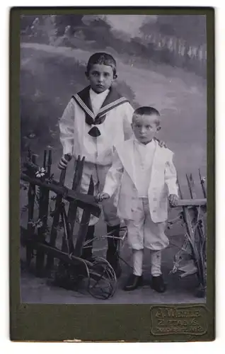 Fotografie A. Wehle, Zittau i. S., Hospitalstr. 2, Portrait zwei freche Buben in Anzügen an einen Holzzaun stehend