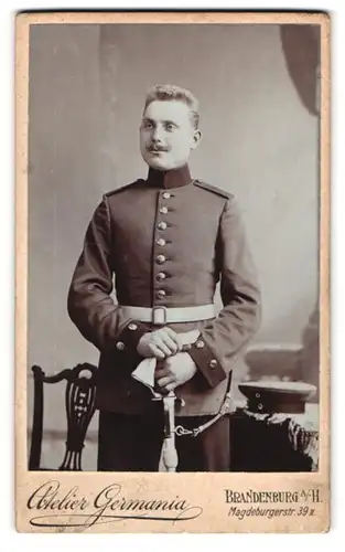 Fotografie Atelier Germania, Brandenburg a. H., Magdeburgerstrasse 39, Soldat in Uniform mit Säbel & verschmitzem Lächeln