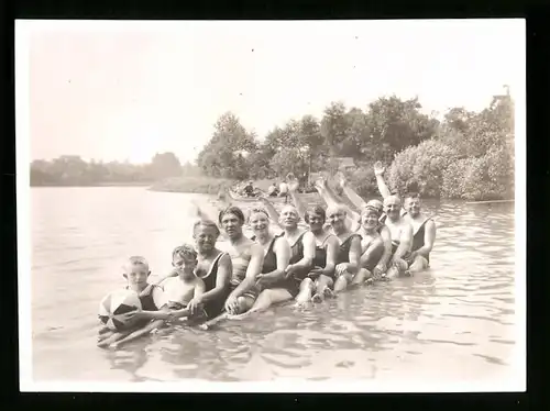 Fotografie Schnappschuss, Herren & Damen in Badebekleidung sitzen in einer Reihe im seichten Wasser