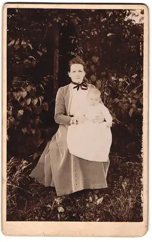 Fotografie unbekannter Fotograf und Ort, junge Mutter im gestreiften Kleid mit Kind auf dem Schoss im Garten, Mutterglück