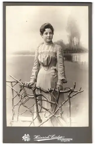 Fotografie Heinrich Cordes, Hildesheim, Zingel 36, Junge Frau in hellem taillierten Kleid vor Landschaftskulisse