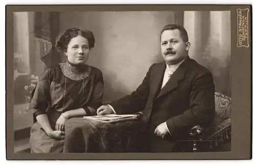 Fotografie Otto Strauch, Zehdenick, Am Markt 1, Bürgerliches Paar mit Fotos am Tisch