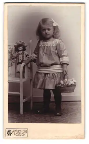 Fotografie A. Wertheim, Rostock, niedliches kleines Mädchen im Kleid mit ihrer Puppe auf der Bank, Puppenkorb