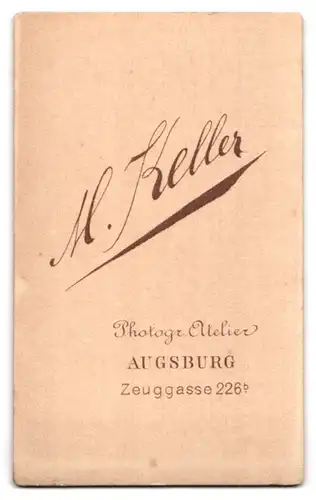 Fotografie M. Keller, Augsburg, Zeuggasse 226b, Elegante Dame mit Spitzenkragen und Medaillon, an einem Tisch sitzend