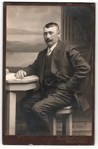 Fotografie Rud. Löbner, München, Portrait stattlicher Herr im eleganten Anzug am Tisch sitzend