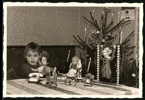 Fotografie Weihnachten, Mädchen mit Spielzeug-Telefon & Puppe neben Weihnachtsbaum