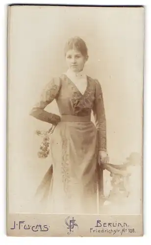 Fotografie J. Fuchs, Berlin, Friedrichstr. 108, Junge Dame in tailliertem Kleid mit dunklen Haaren und leichtem Lächeln