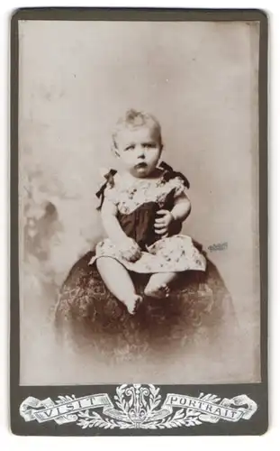 Fotografie Visit Portrait, Ort unbekannt, Kleinkind trägt ein mit Stickereien und Bändern verziertes Kleid