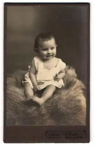 Fotografie H. Deike, Hannover-Linden, Portrait lachendes kleines Mädchen auf einem Fell sitzend