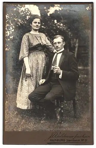 Fotografie J. Waldemar Jacobsen, Hamburg, Steindamm 51, Mann im Anzug mit Zigarre in der Hand sitzt neben Frau im Kleid