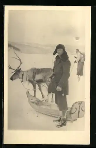 Foto-AK Finne mit einem Rentierschlitten, Im Hintergrund Skifahrer