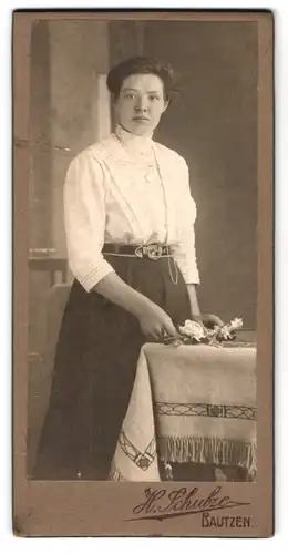 Fotografie H. Schulze, Bautzen, Junge Dame mit Rock und weisser Bluse steht an einem Tisch