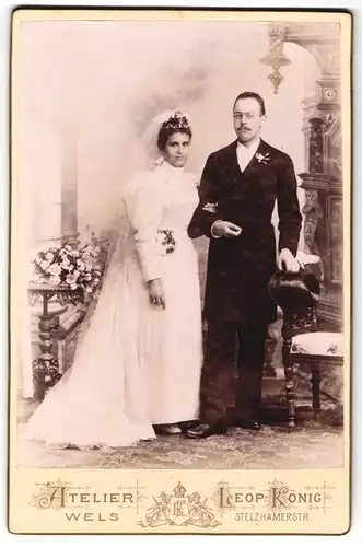 Fotografie Leop. König, Wels, junges Ehepaar im Hochzeitskleid und im Anzug mit Zylinder
