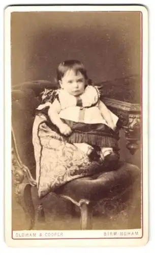 Fotografie Oldham & Cooper, Birmingham, 82 New Street, Niedliches Kind im weiss-schwarzen Kleid schmollt auf einem Kissen
