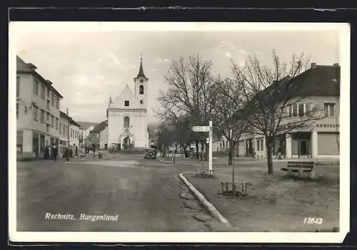 AK Rechnitz, Strassenpartie mit Kirche und Geschäften